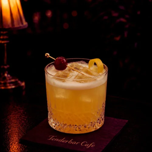 Whisky Sour koktel u lowball čaši sa ledom, viski, limunov sok i sirup, sa penušavom teksturom i ukrasom od višnje ili limuna.
